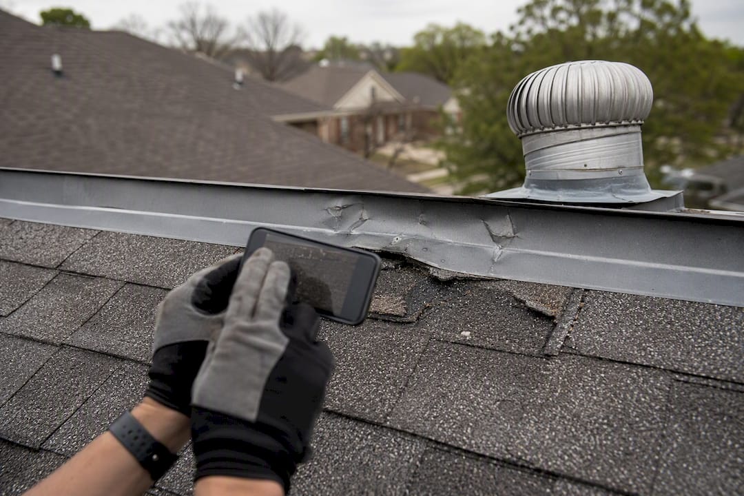 Hand taking photos of hail damage on roof